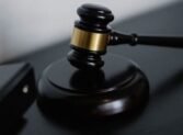 High angle of shiny wooden ceremonial mallet with golden detail placed on judge tale near documents folders